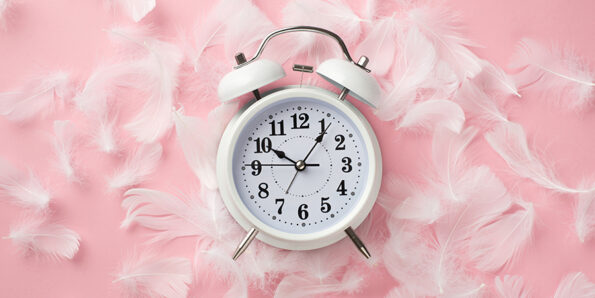 13 formas eficaces de mejorar la calidad del sueño - Top view photo of white alarm clock and pink feathers on isolate