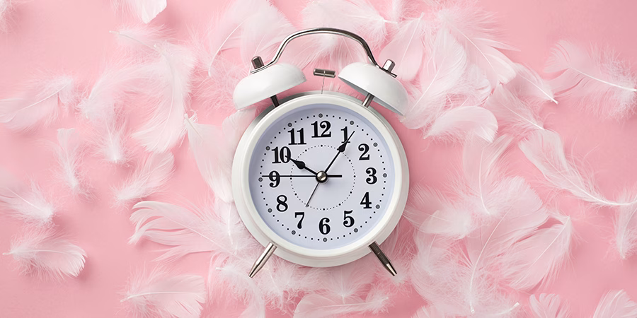 13 formas eficaces de mejorar la calidad del sueño - Top view photo of white alarm clock and pink feathers on isolate